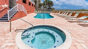 Un espace piscine comprenant un jacuzzi, des chaises longues et un escalier menant à un niveau supérieur.