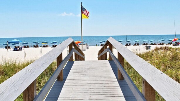 A wooden boardwalk leading to a beach with umbrellas and lounge chairs.