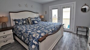 A bedroom with a bed, nightstands, a dresser, a ceiling fan, and a balcony door.