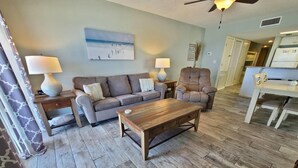 A living room with a sofa, armchair, coffee table, and a dining table with chairs. - Westwind 301 (Gulf Shores)