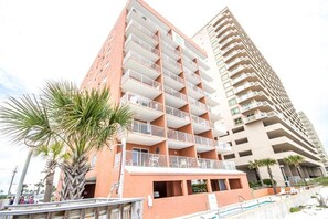 Un edificio de varios pisos con balcones, un techo plano y una palmera en primer plano.