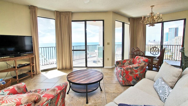 A spacious living room with a flat-screen TV, a round coffee table, and two sofas with floral upholstery. - Phoenix East 1201 (Orange Beach)