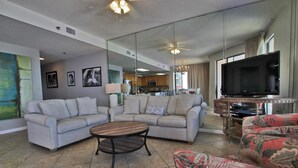 A living room with a sectional sofa, a coffee table, a TV, and a kitchen in the background. - Phoenix East 1201 (Orange Beach)