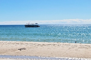 A beach with a boat in the water and a person standing on the sand. - Summerchase 1108 (Orange Beach)