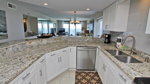 A modern kitchen with granite countertops, white cabinets, stainless steel appliances, and a large island. - Summerchase 1108 (Orange Beach)