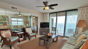 A spacious living room with a ceiling fan, a television, and a large window offering a view of the ocean. - Summerchase 1108 (Orange Beach)