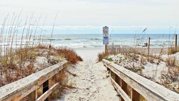A wooden boardwalk leading to the beach with a signpost in the distance.