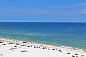 Ein Strand mit Reihen von Liegestühlen und Sonnenschirmen, ein sandiger Uferstreifen und der Ozean.