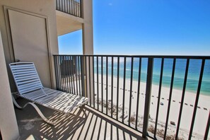 Un balcon avec une chaise en métal blanche et une vue sur une plage de sable et une eau d’un bleu limpide.