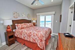 A bedroom with a bed, nightstands, a desk, a ceiling fan, and a view of the ocean. - Our Point of View #3 (Gulf Shores)