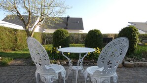 Un patio con dos sillas blancas de metal ornamentado y una mesa redonda pequeña.