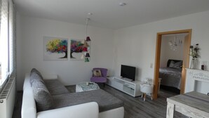 Una sala de estar moderna con un sofá seccional, un televisor de pantalla plana, una pequeña mesa de comedor y una chimenea blanca.