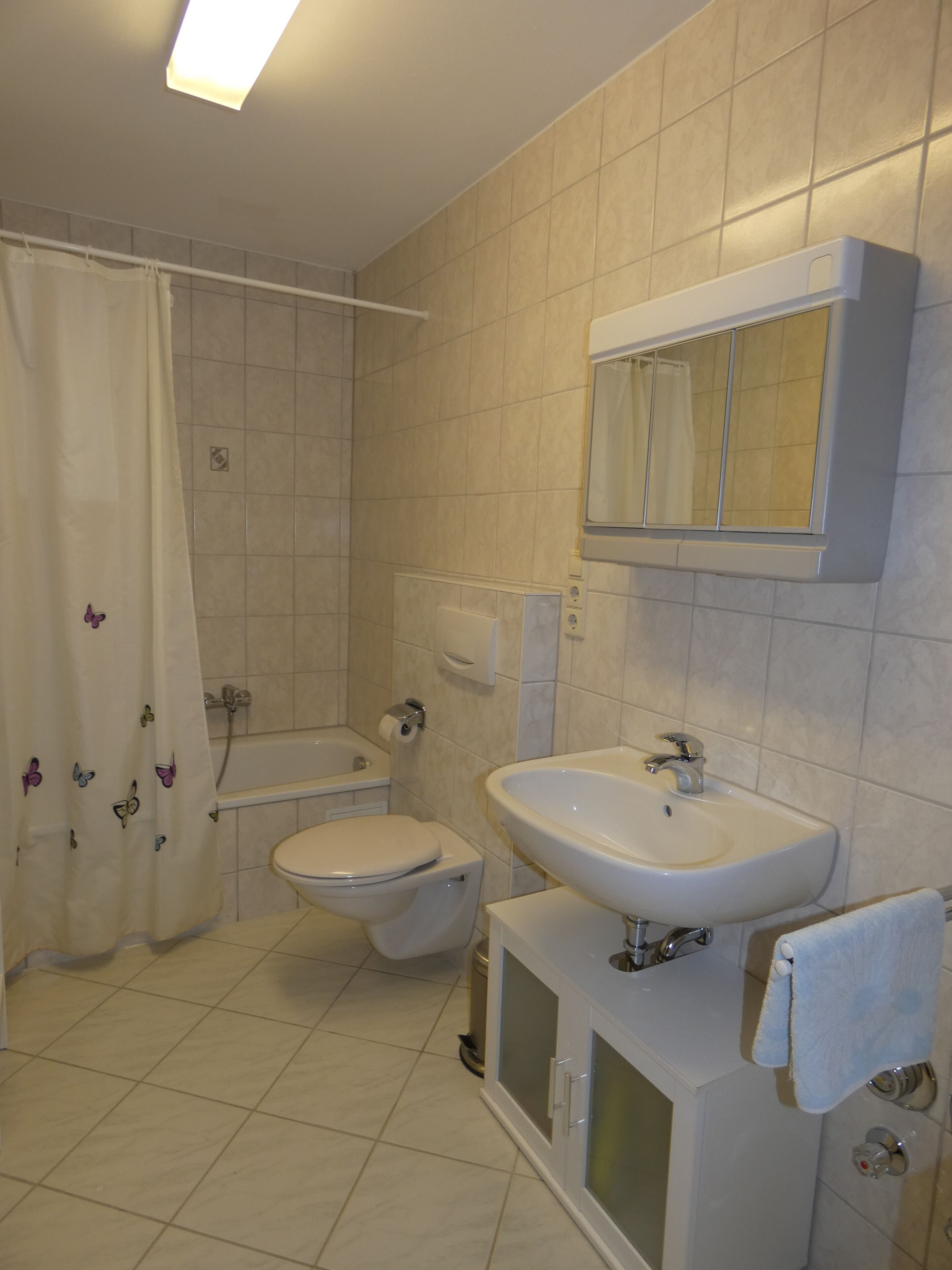 A bathroom with a toilet, sink, bathtub, and a shower curtain with butterfly designs.