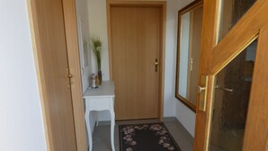 Un pasillo con una puerta de madera, un escritorio blanco, un espejo y un tapete con motivos florales.