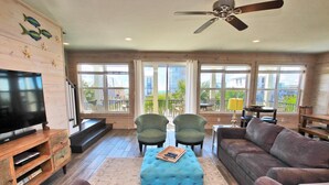 A spacious living room with a television, two armchairs, a sofa, and a ceiling fan. - Serendipity Sands (Gulf Shores)