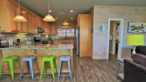 A kitchen with wooden cabinets, a granite countertop, and three green stools. - Serendipity Sands (Gulf Shores)