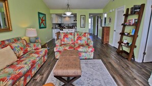 A living room with a sofa, a coffee table, and a rug. There is a kitchen in the background. - Palmetto 306 (Orange Beach)