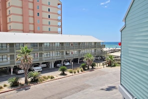 A multi-story hotel with a flat roof, parking area, and a view of the beach.