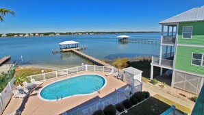 A pool area with a clear view of the water, a dock, and a building with a balcony. - On Golden Pond 8A West (Gulf Shores)