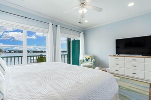 A bedroom with a large bed, a TV, a chair, and a view of a body of water. - On Golden Pond 8A West (Gulf Shores)