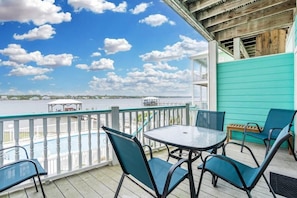 A covered outdoor area with a table and chairs, overlooking a body of water and a distant shoreline. - On Golden Pond 8A West (Gulf Shores)