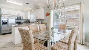 A modern kitchen with white cabinets, stainless steel appliances, and a glass dining table with wicker chairs. - On Golden Pond 8A West (Gulf Shores)