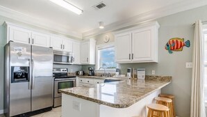 A kitchen with white cabinets, stainless steel appliances, a granite countertop, and wooden stools. - On Golden Pond 8A West (Gulf Shores)