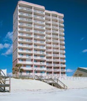 A multi-story hotel with balconies, located near a beach.