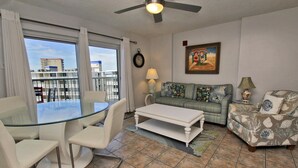 A living room with a glass table, white chairs, a sofa, and a patterned armchair. - Tradewinds 807 (Orange Beach)