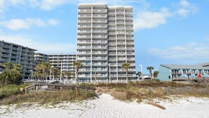 A high-rise hotel with multiple balconies, situated on a beach with a wooden boardwalk leading to the entrance. - Tradewinds 807 (Orange Beach)
