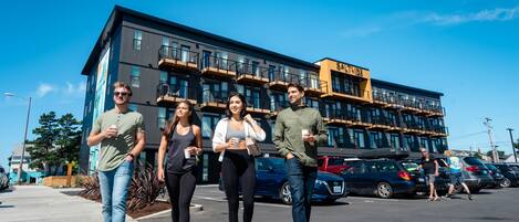 En grupp människor går på en trottoar framför en byggnad med flera balkonger och en skylt med texten ”SAAL”.