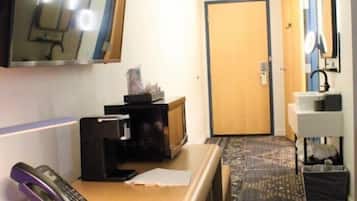 Habitación de hotel con escritorio, teléfono, microondas, televisor pequeño, puerta y espejo.