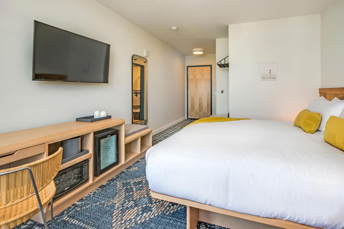 A hotel room with a large bed, a flat-screen TV mounted on the wall, a desk with a computer, and a chair.