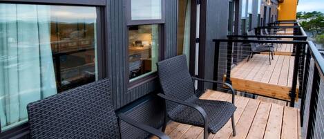 A modern building with a wooden deck, black metal railings, and wicker furniture.