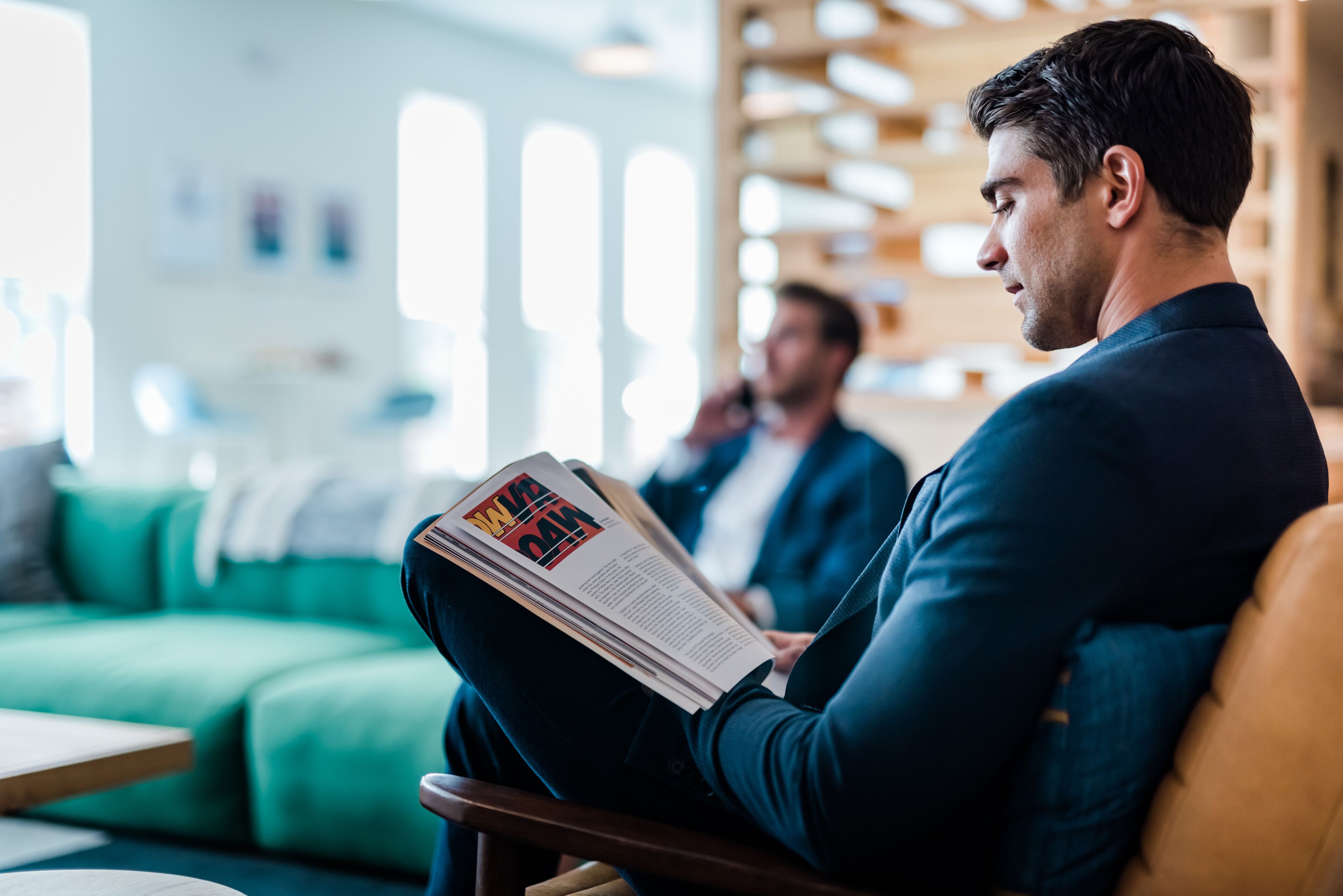 Un hombre leyendo una revista en una habitación moderna y luminosa, con un sofá verde y muebles de madera.