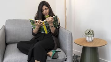 A person sitting on a grey sofa reading a book, with a small round table with a plant beside them.