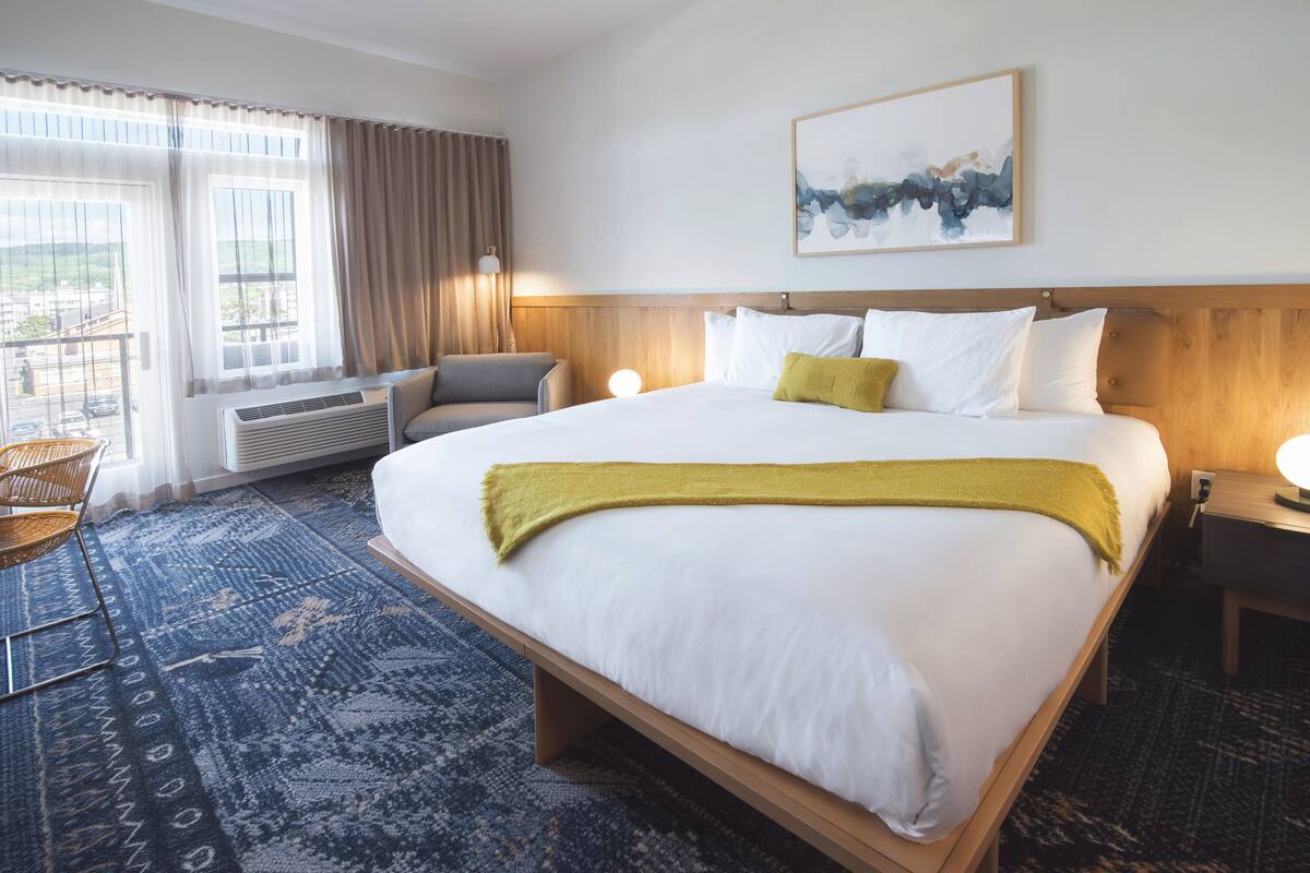 A hotel room with a large bed, a chair, a desk, and a window with curtains.