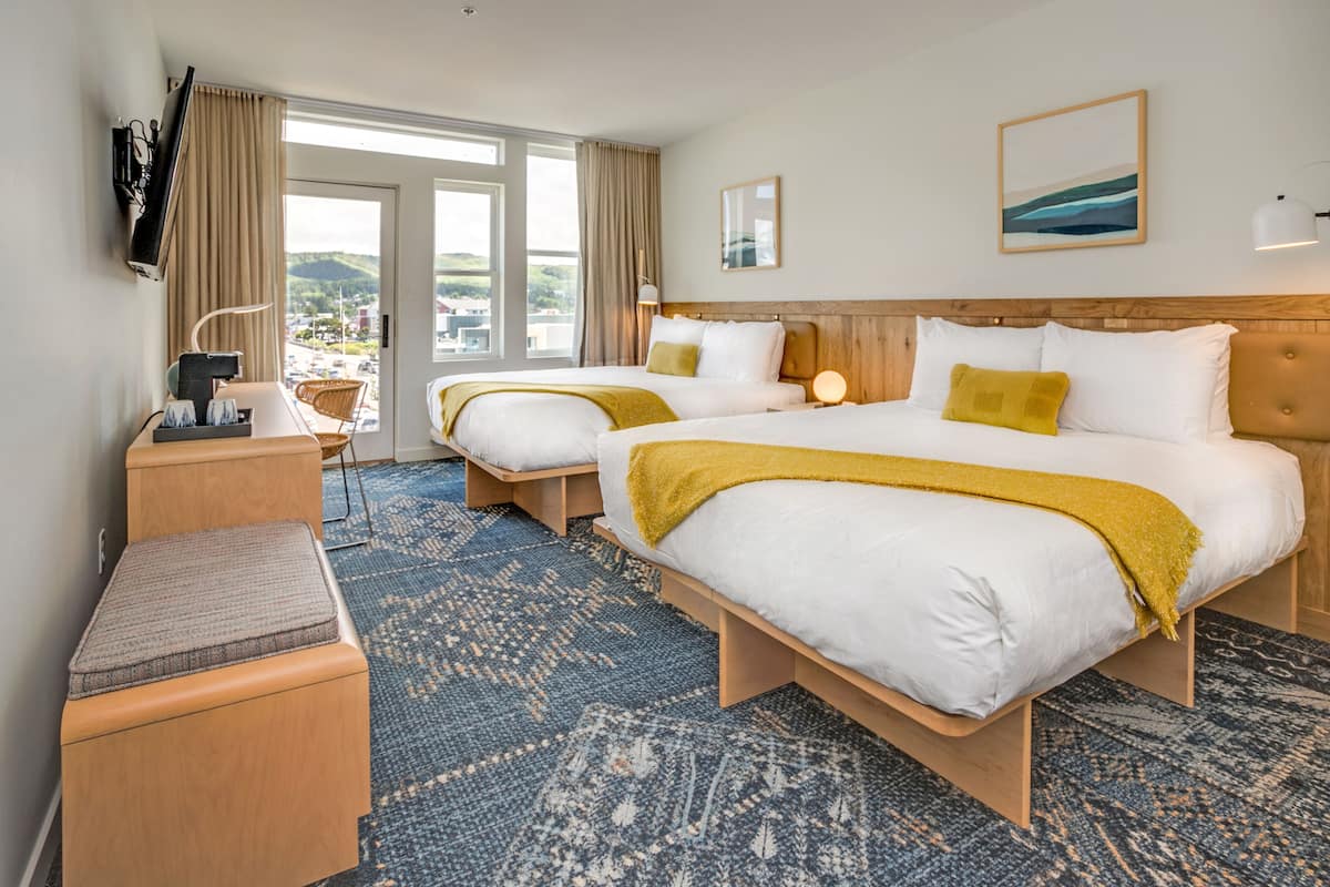 A hotel room with two beds, a desk, and a chair.