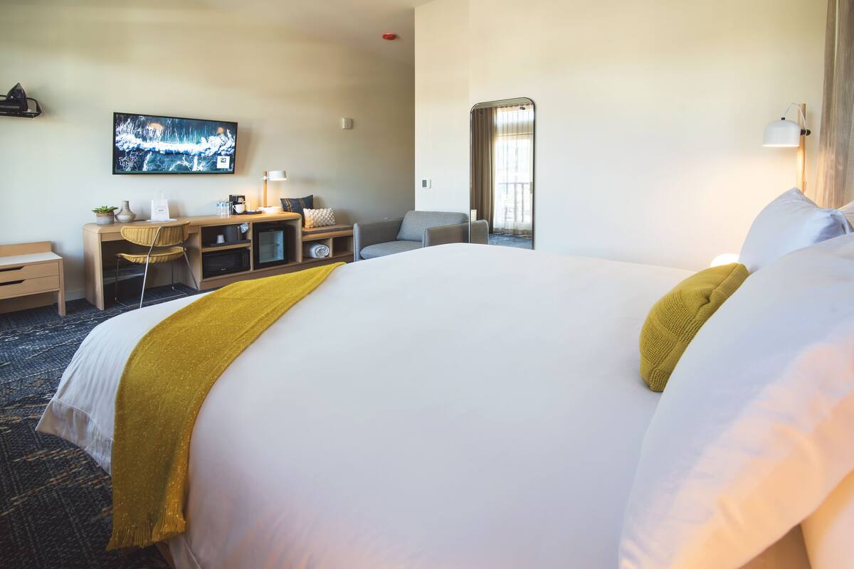 A hotel room with a large bed, a desk with a chair, a television, and a mirror.