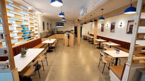 Un intérieur de restaurant moderne avec des lambris en bois, des luminaires suspendus bleus et un comptoir central.