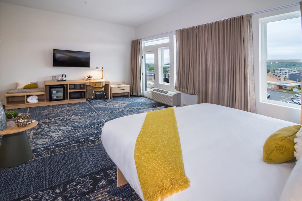 A hotel room with a large bed, a desk, a TV, and a view of the city.