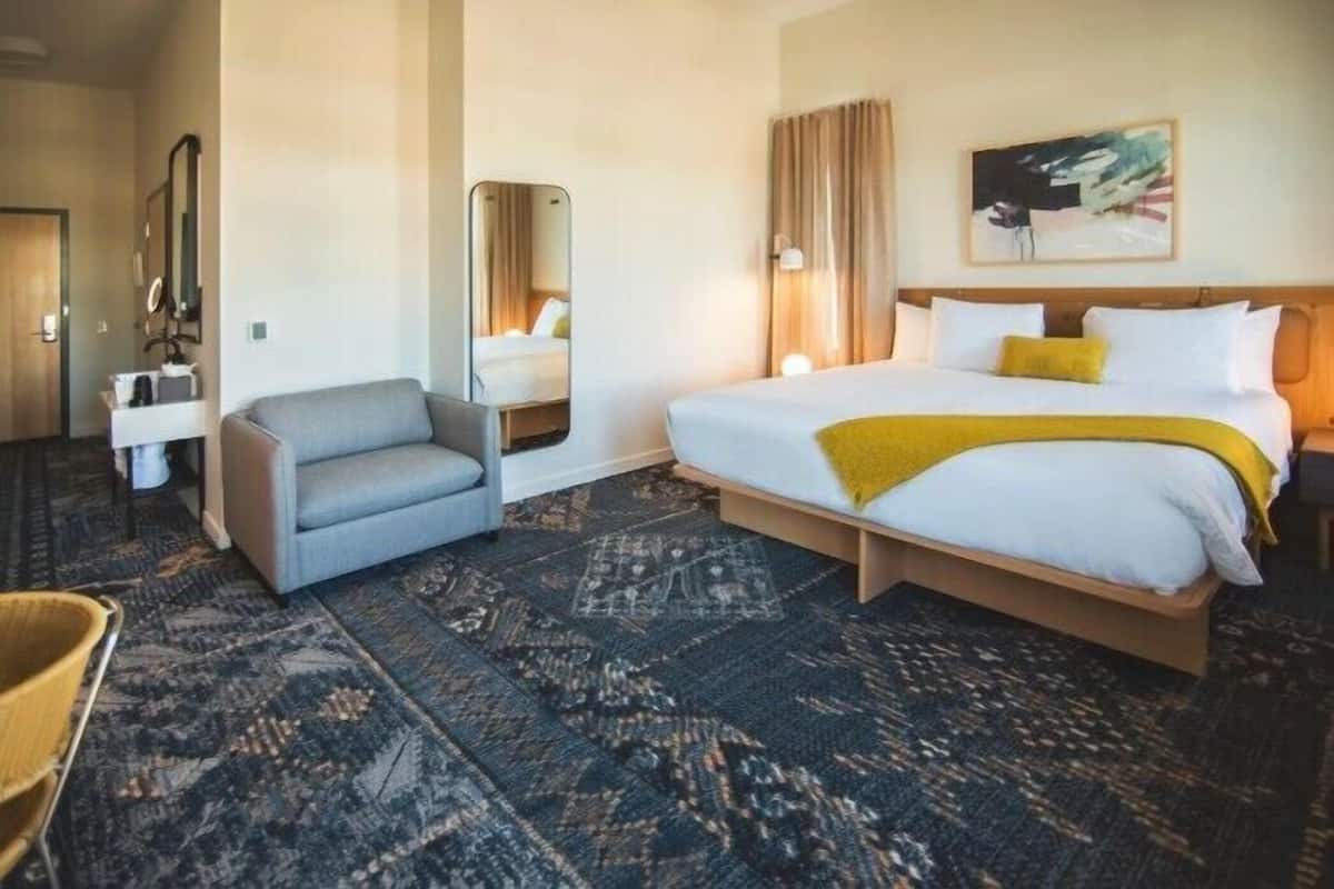 A hotel room with a bed, a chair, a desk, and a mirror.