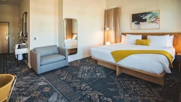 A hotel room with a bed, a chair, a desk, and a mirror.