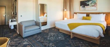 A hotel room with a bed, a chair, a desk, and a mirror.