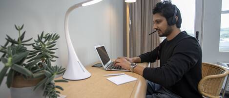 A man working at a desk with a laptop, a white desk lamp, a potted plant, and a newspaper.