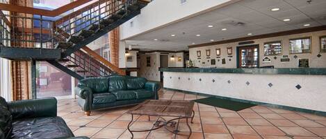 A lobby with a staircase, leather sofas, a wooden coffee table, and a reception desk with framed awards.