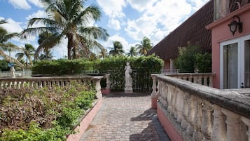 A paved pathway leading to a building with a red-tiled roof, surrounded by palm trees and a stone balustrade.