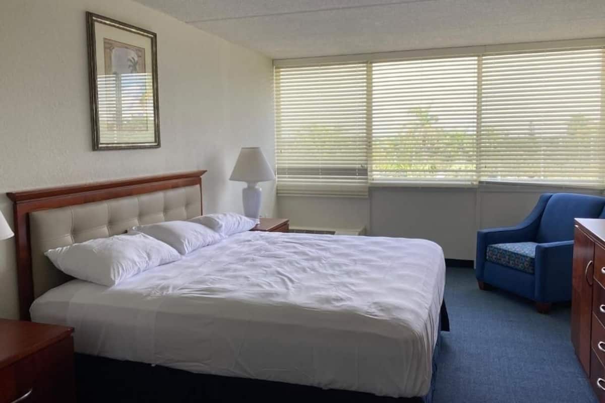 A hotel room with a large bed, a nightstand, a lamp, a chair, and a dresser.