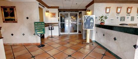 A hotel lobby with a tiled floor, a reception desk, and a sign directing to the elevator and first floor rooms.