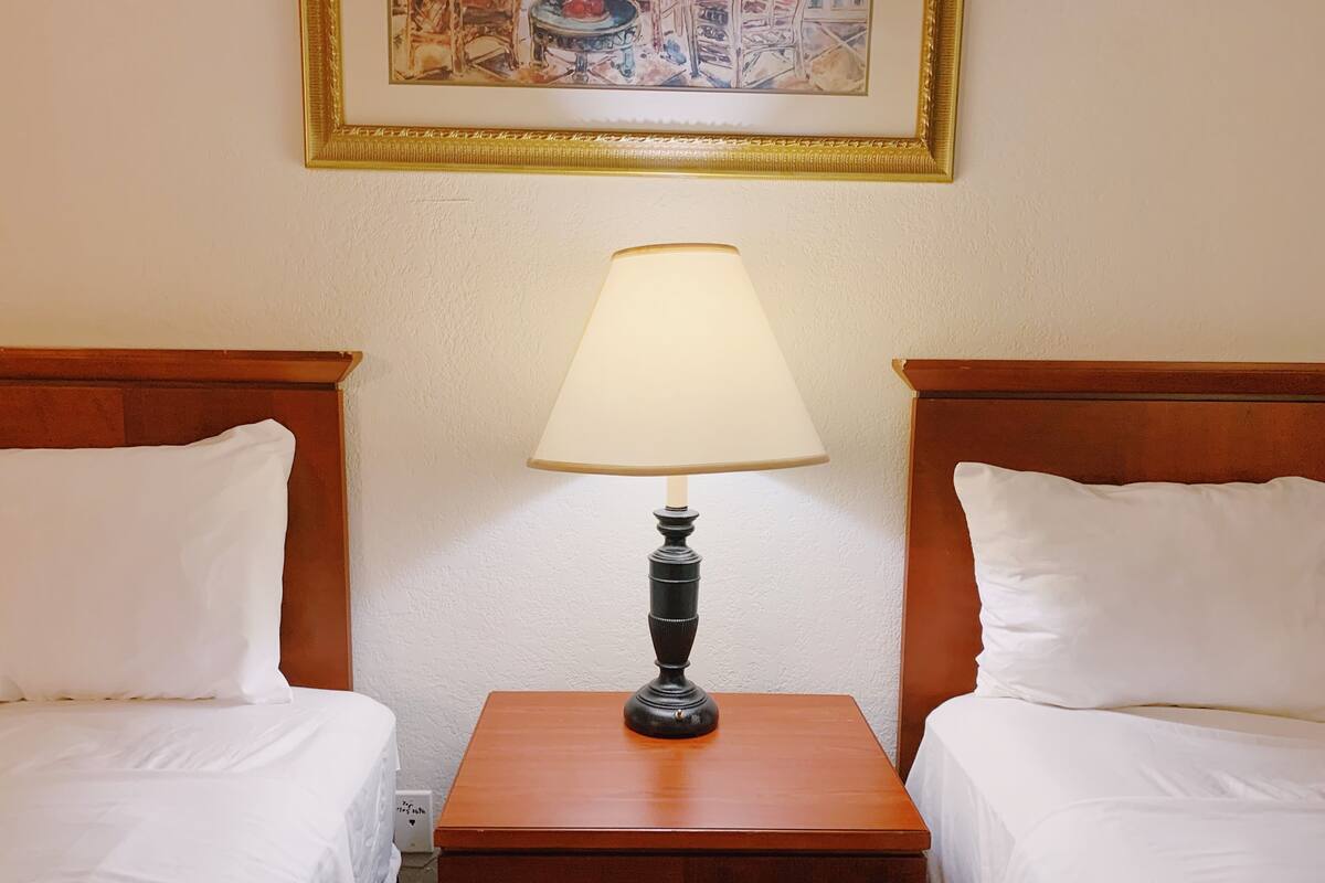 A hotel room with two single beds, a nightstand with a lamp, and a framed picture on the wall.